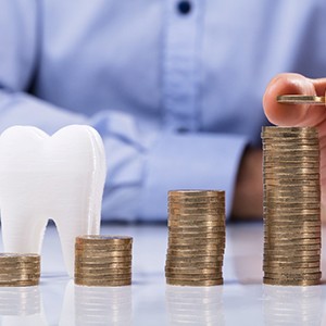 Model tooth and coin stacks representing cost of dental implants in Colorado Springs