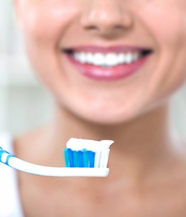 Smiling woman holding toothbrush with toothpaste on the bristles