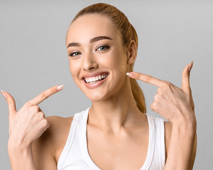 Woman in white tank top pointing to her healthy smile