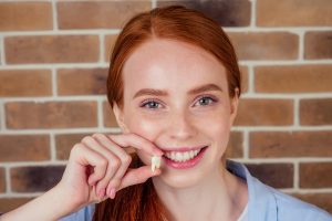 Young woman holding extracted wisdom tooth and smiling